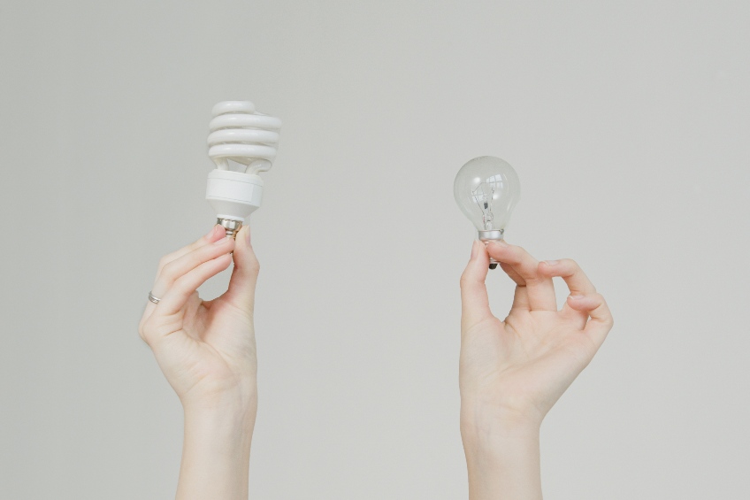 One hand holding up an energy efficient lightbulb, one hand holding an incandescent light bulb.